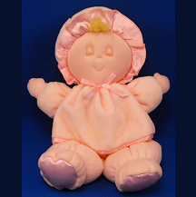 A photo of a smiling pink plushie doll with closed eyes, sitting against a blue background. The doll has a pink dress and a few strands of blonde hair peeking out from under a pink bonnet hat.